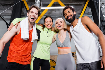 cheerful multiethnic people looking at camera while embracing in gym