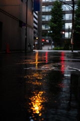 オレンジと赤いライトが映り込んだ雨に濡れたアスファルト