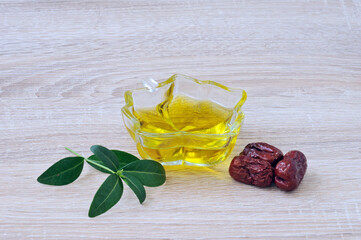 Jojoba fruits on the background of a cup with oil and green leaves. Selective focus on the anterior surface of the fruit.