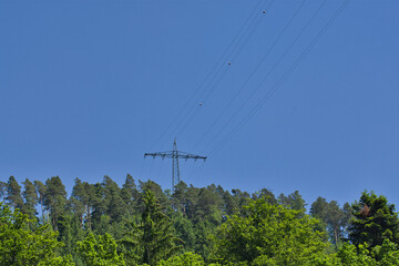 Teleaufnahme einer Hochspannungsleitung auf einem Berg mit einem Wald im Vordergrund