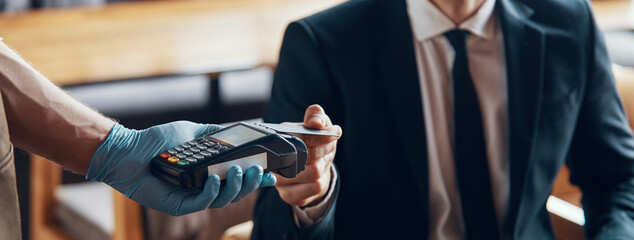 Close-up of handsome young smiling man in full suit making a contactless payment