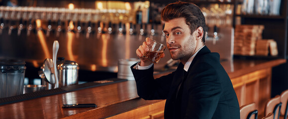 Handsome young man in full suit holding glass with alcohol drink
