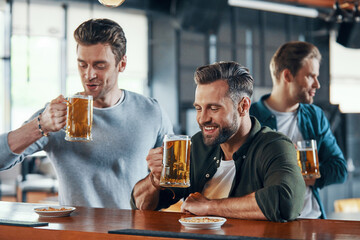 Group of cheerful young men in casual clothing enjoying beer and communicating