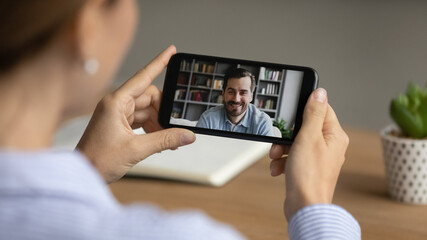 Back rear close up young female worker holding distant video call conversation with male partner using mobile software application, discussing working issues distantly or communicating with friend.