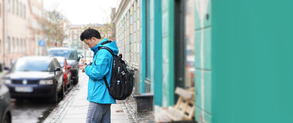 Asian man blue jacket backpack travel to Europe lost searching street on internet mobile