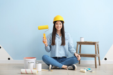 Young woman with roller and cans of paint near color wall