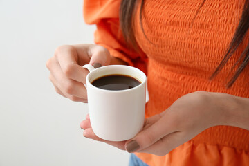 Young woman drinking coffee on light background, closeup