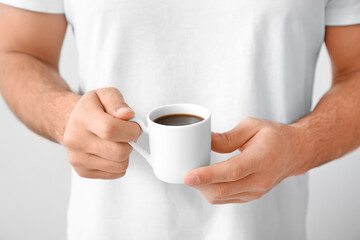 Young man with cup of coffee on light background, closeup