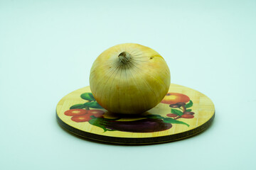 Close-up onion lies on a rustic round wood plate on the white background. Village vegetable is good for diet it contains vitamins and microelements. Landscape orientation picture, copy space.