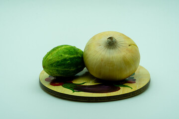 Onion and deformed cucumber lie on a rustic wood plate on the white background.  Organic vegetables...