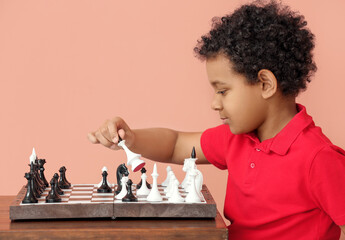 Cute African-American boy playing chess on color background