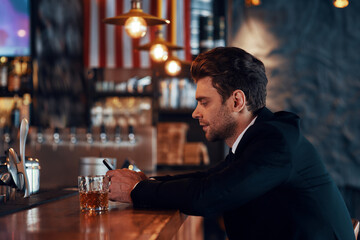 Side view of handsome young man in full suit using smart phone