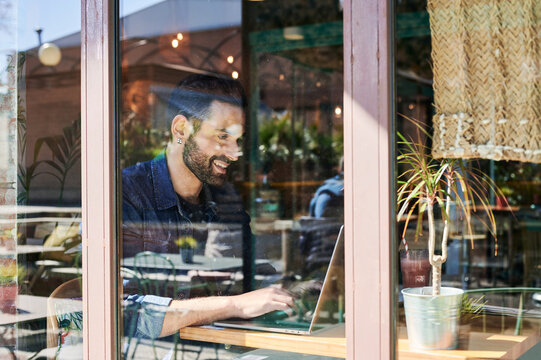 Man ethnic entrepreneur typing on laptop in restaurant