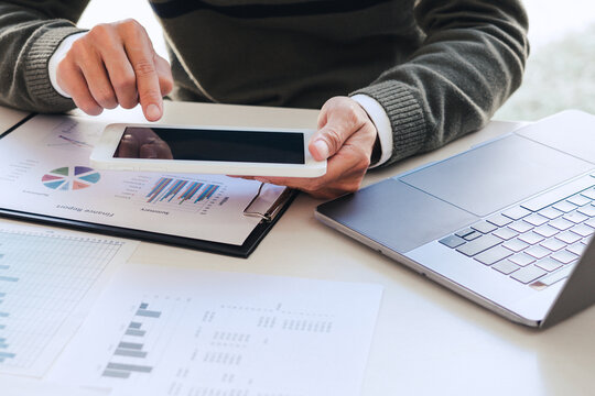A male freelancer using mobile phone collecting information analyzing the data in chart for marketing research