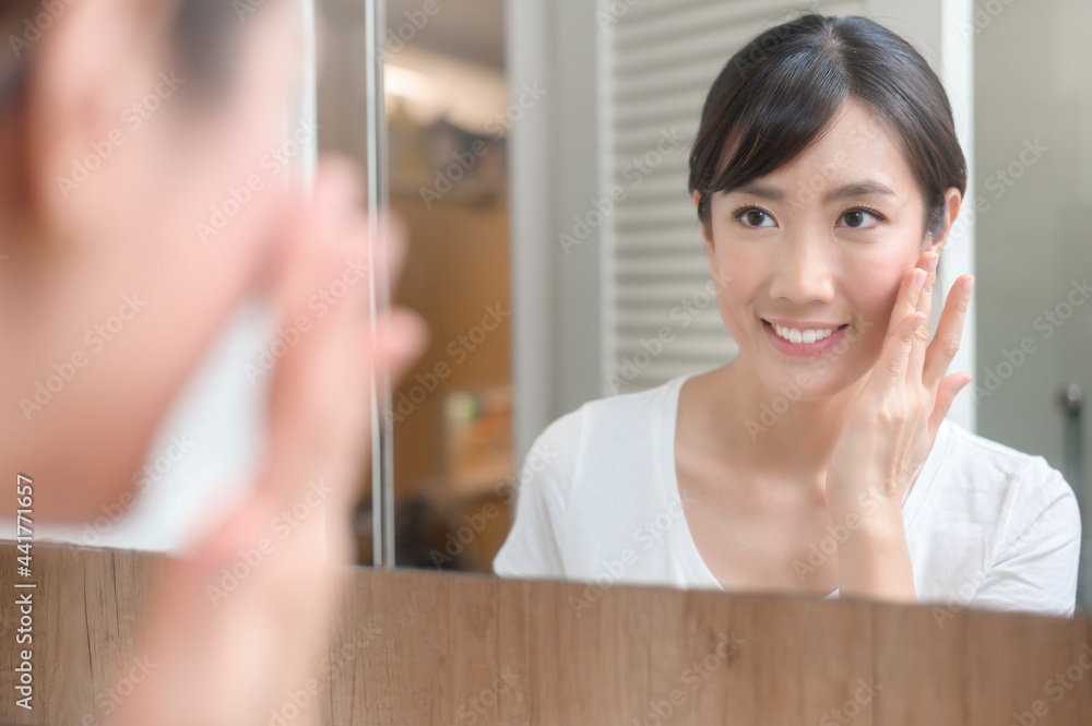 Wall mural happy beautiful woman applying moisturizing cream on face, skin care and treatment concept