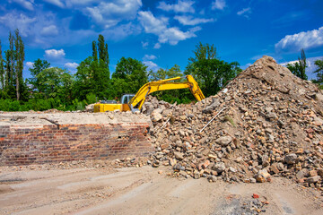 yellow excavator doing demolition work on a construction site. Also called diggers, JCB, mechanical...