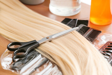 Strand of blonde hair and scissors on table, closeup
