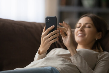 Focus on smartphone in hands of relaxed beautiful woman lying on cozy couch. Addicted to modern...