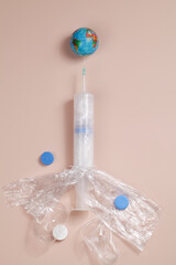 Environmental pollution problem. Planet Earth on syringe filled with plastic on beige background. Concept of dependence on plastic.