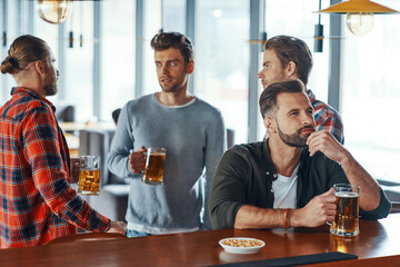 Group of young men in casual clothing enjoying beer and communicating