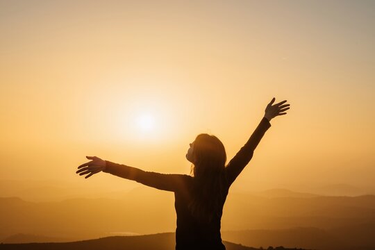 Carefree woman standing on hill and enjoying freedom with outstretched arms