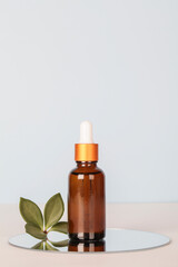 dark amber glass bottle with oil on mirror with green leaf on blue background. copy space. Beauty concept, brand packaging mock up.