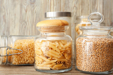 Glass jars with raw pasta and wheat grains on wooden background