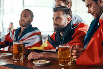 Group of young men covered in international flags enjoying beer