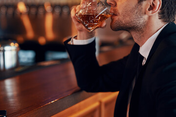 Close-up of young man in suit drinking whiskey while sitting at the bar counter in restaurant