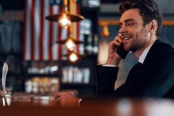 Side view of handsome young man in full suit talking on smart phone