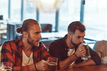 Young men in casual clothing enjoying beer while sitting at the in the pub together