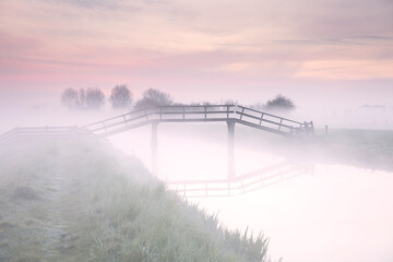 wooden bike bridge over river at sunrise in fog