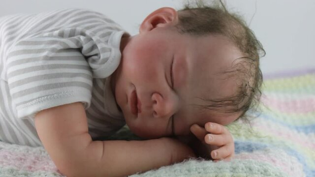 Sleeping baby boy wearing stiped vest and lying on knitted blanket represented by a reborn doll