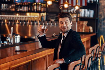 Handsome young man in full suit holding glass with alcohol drink