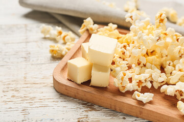 Board with tasty popcorn and butter on light wooden background, closeup