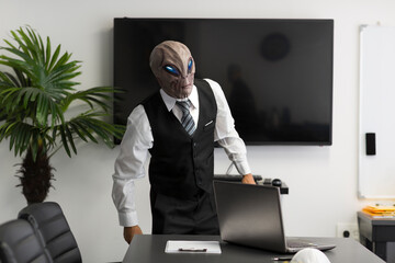A humanoid Alien in a white shirt, business suit looking at camera in the office with laptop....
