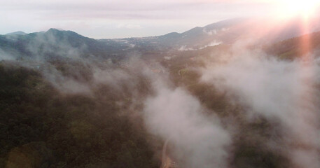 Fototapeta premium AERIAL. Flying above the clouds over road and rice terraces in Thailand at sunset