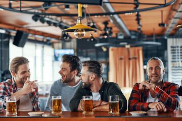 Group of cheerful young men in casual clothing enjoying beer and communicating