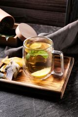 Wooden board with cup of tasty green tea and ingredients on dark table