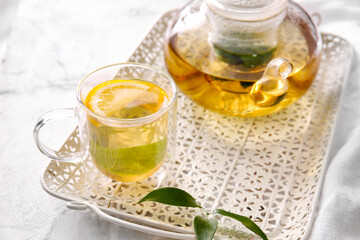 Tray with cup of tasty green tea and pot on light table