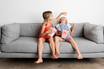 Two young girls sitting on sofa feeding popcorn to each other