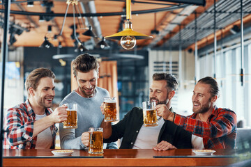 Happy young men in casual clothing toasting each other with beer and smiling