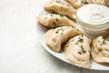 Plate with tasty dumplings and sour cream on light background, closeup