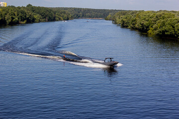 Speedboat towing an athlete on a Board against the background of the forest. Athlete water skiing...