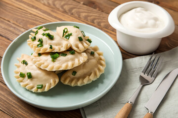 Plate with tasty dumplings and sour cream on wooden background