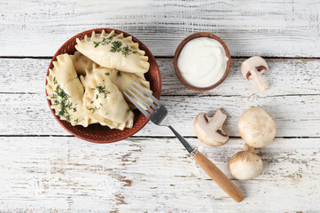 Obraz na płótnie Canvas Bowl with tasty dumplings, sour cream and mushrooms on light wooden background
