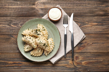 Fototapeta premium Plate with tasty dumplings and sour cream on wooden background