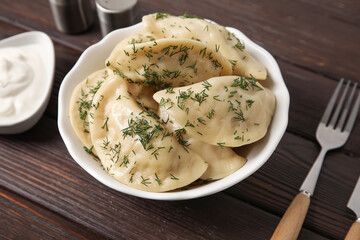 Plate with tasty dumplings and sour cream on dark wooden background