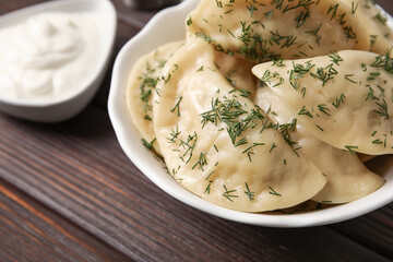 Plate with tasty dumplings and sour cream on dark wooden background, closeup