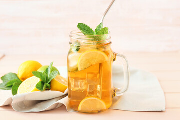 Mason jar of tasty ice tea with fruits on light wooden background